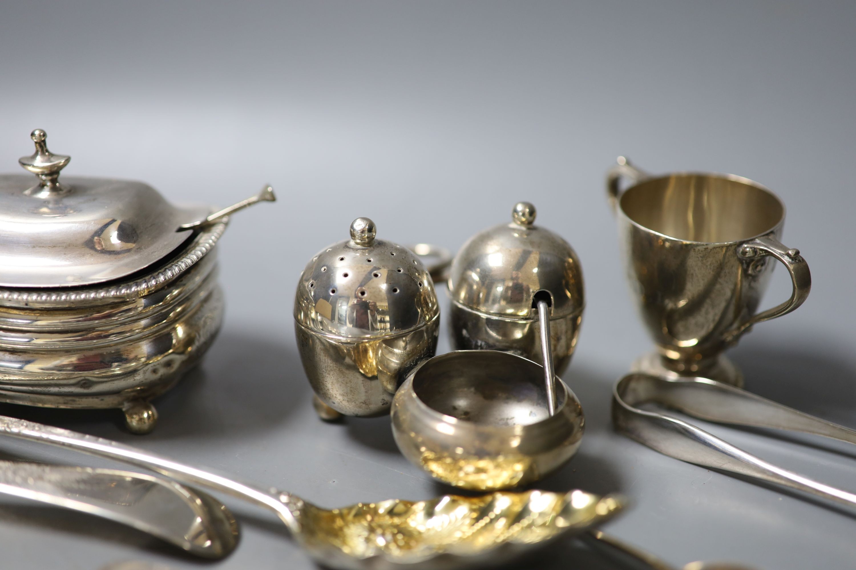 A group of small silver including a Georgian silver mustard, marks rubbed, a pair of Georgian silver berry spoons, two continental spoons, a small Victorian silver cruet stand, a tea strainer on stand, napkin ring, small